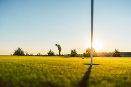 Full length view of the silhouette of a male player, hitting a long shot on the putting green of a professional golf course of a modern country club (Kzenon)